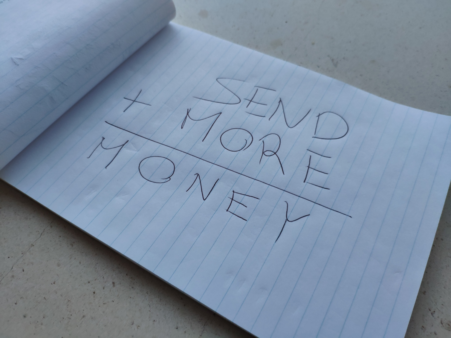 Um pedaço de papel onde se vê a soma "SEND + MORE = MONEY".