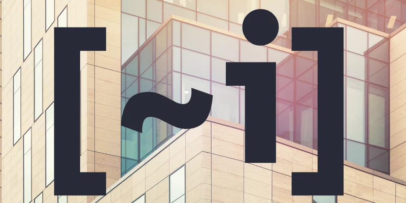 The text “~i” inside a pair of square brackets in front of a highly geometrical building.