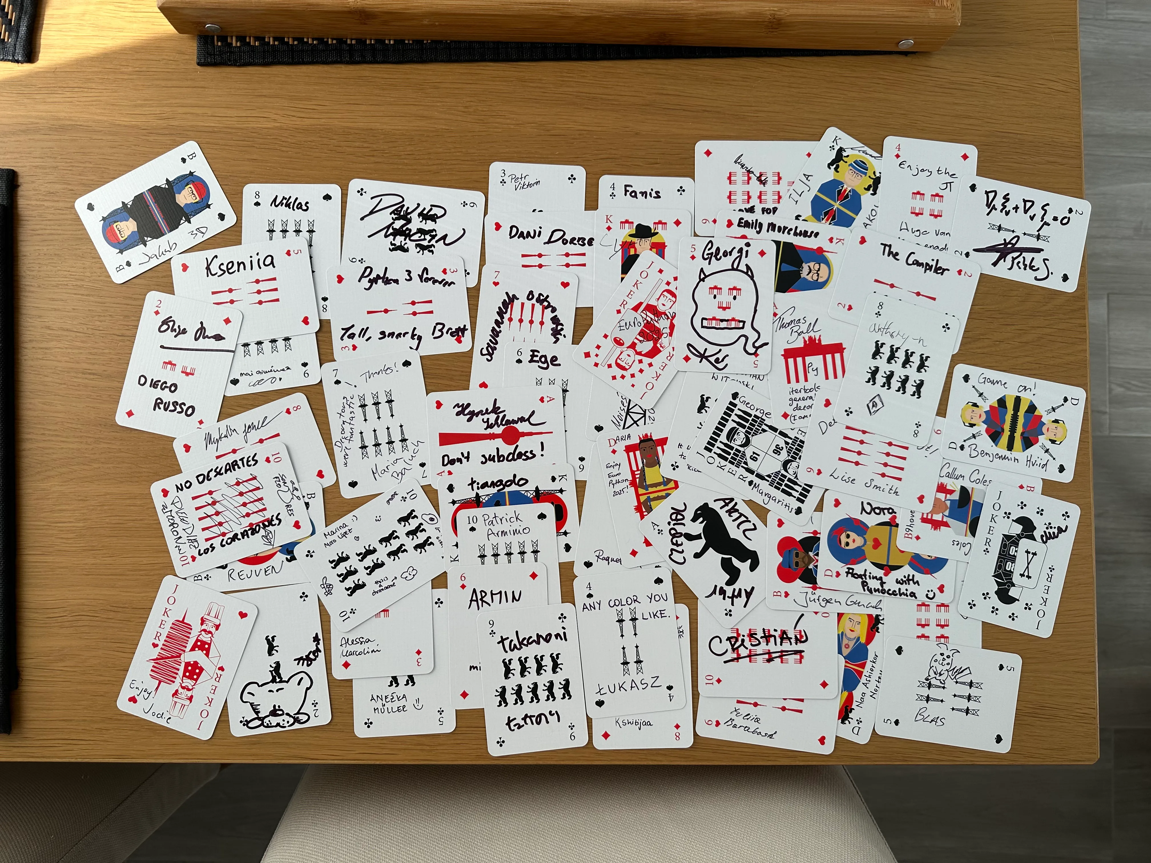 A picture of a deck of cards with the cards all scattered on top of a table. All cards seem to be scribbled, and upon closer inspection you can tell that the cards are actually signed.