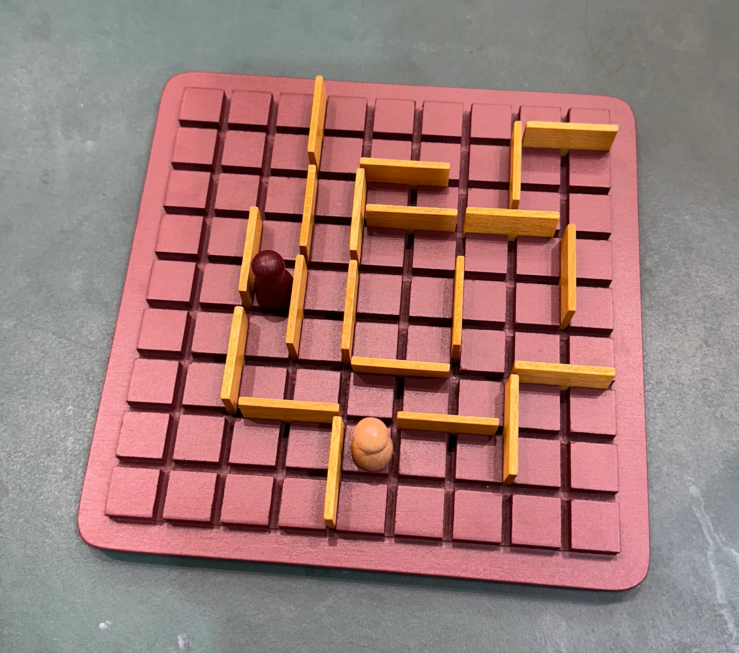 A picture of a Quoridor board of a game that is almost over. The light pawn is one move away from reaching the bottom of the board while the dark pawn is four moves away.