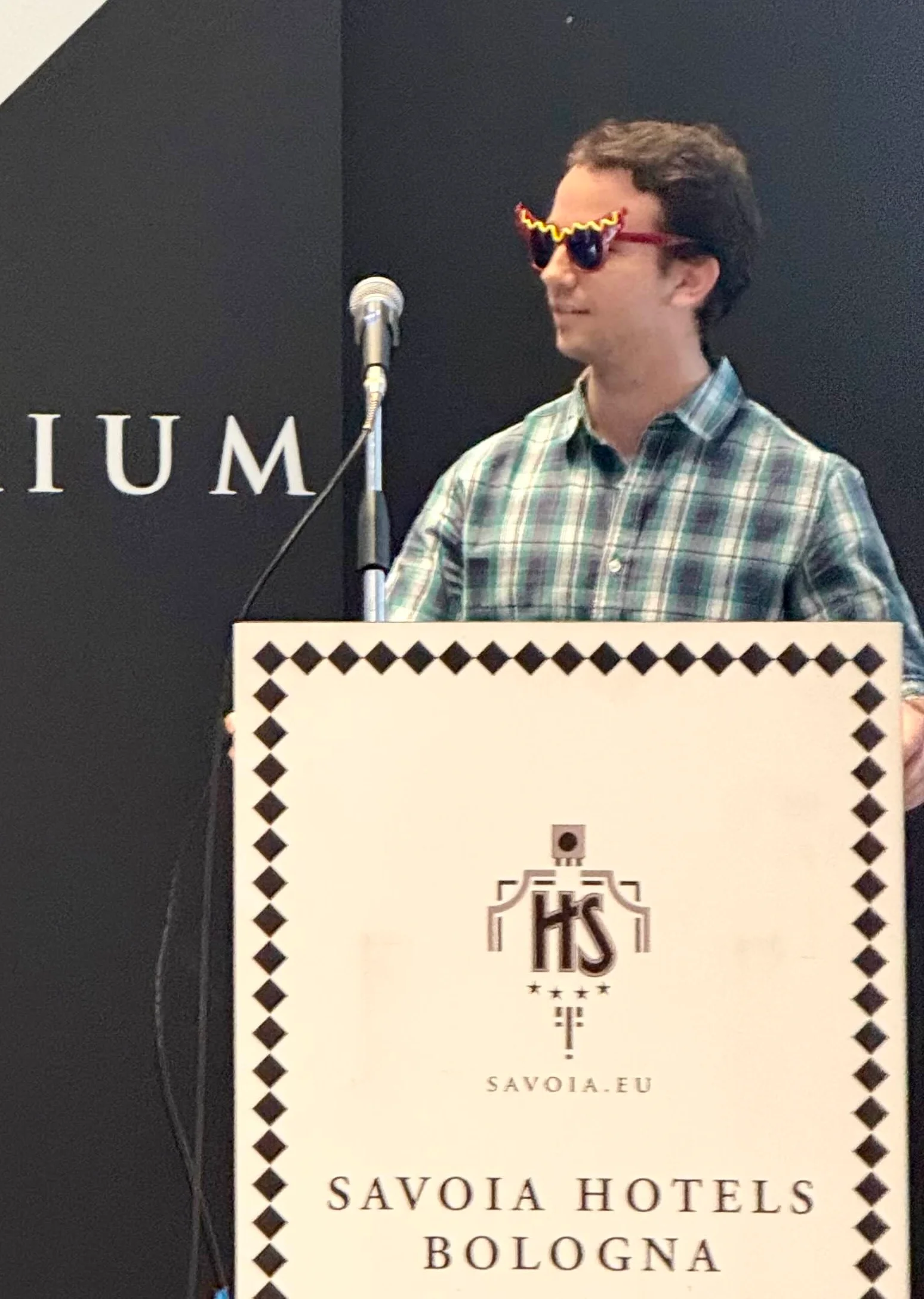 A photo of Rodrigo giving a talk while wearing some red glasses with the shape of a sausage with mustard on top.