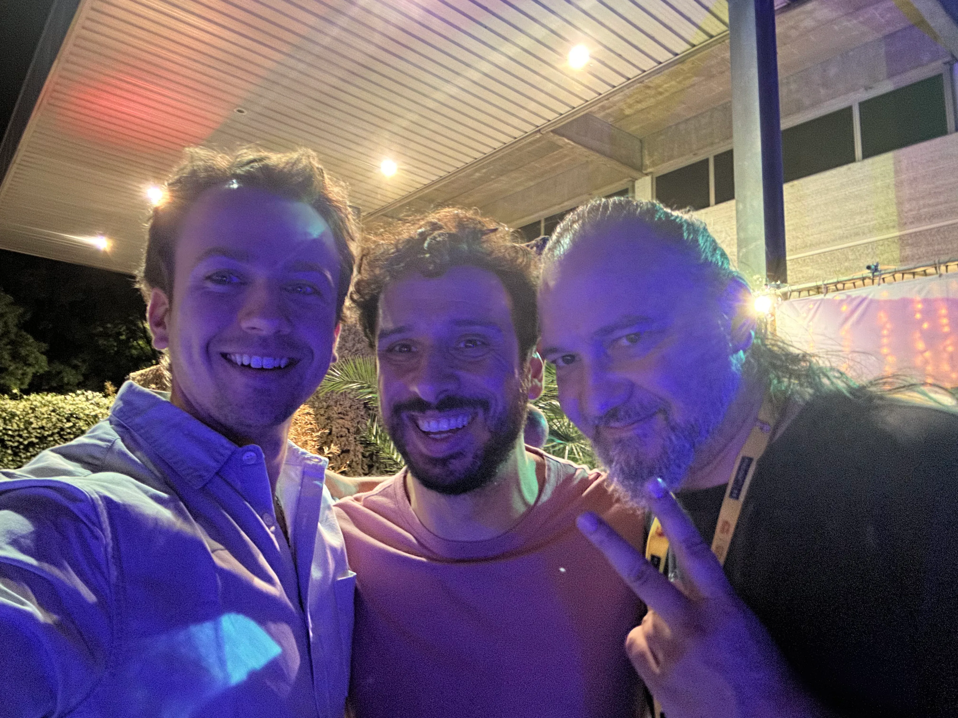 Rodrigo and two PyCon Italy organises smiling in a close-up photograph. The lighting of the photo is bad because of the party-like ambiance of the venue.