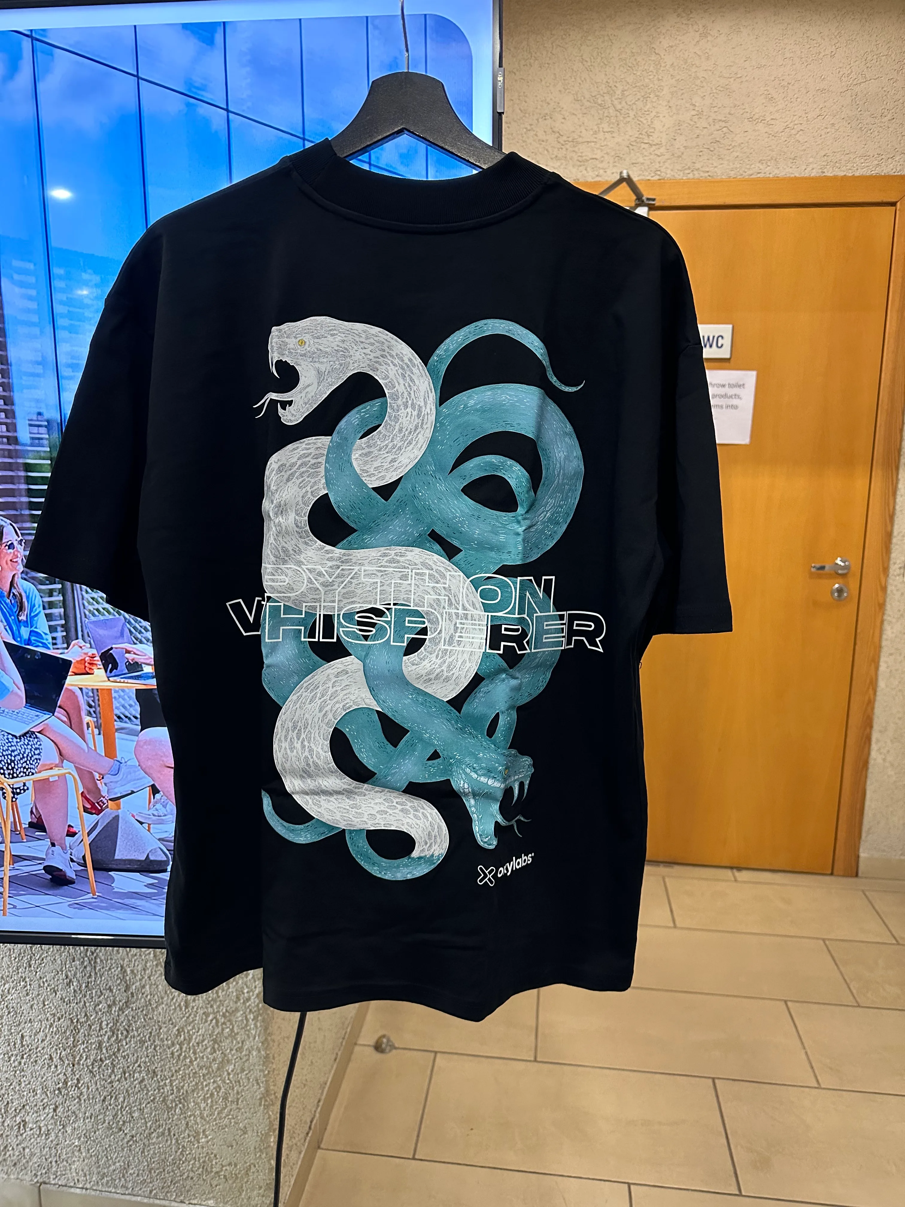 The Python Whisperer t-shirt. The back of a t-shirt showing two entangled snakes with the words “Python Whisperer” at the bottom.